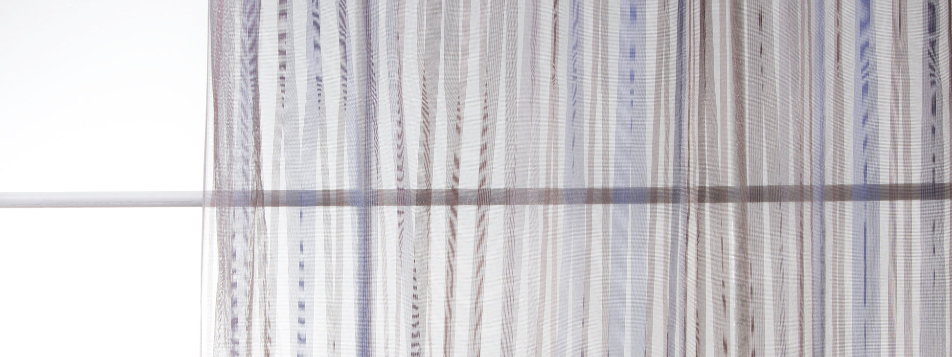 Vertical sheer drapery panels in white and light-gray striped fabric, light-filtering window treatment.