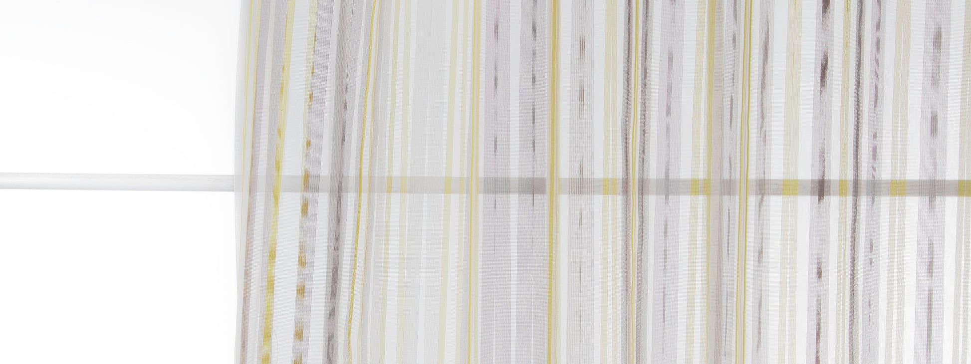 Vertical striped sheer curtain in white, gray & pale yellow with flowing folds by a window.