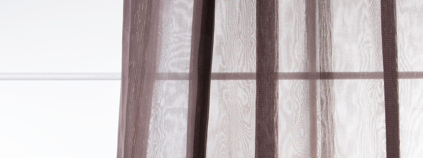 Brown sheer curtains in translucent fabric with vertical folds hanging over a window.