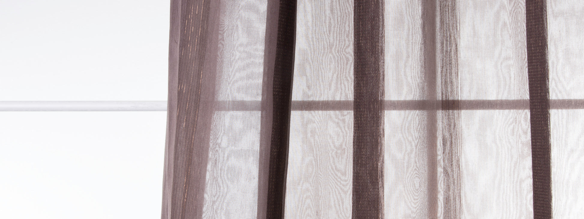 Brown sheer curtains in translucent fabric with vertical folds hanging over a window.