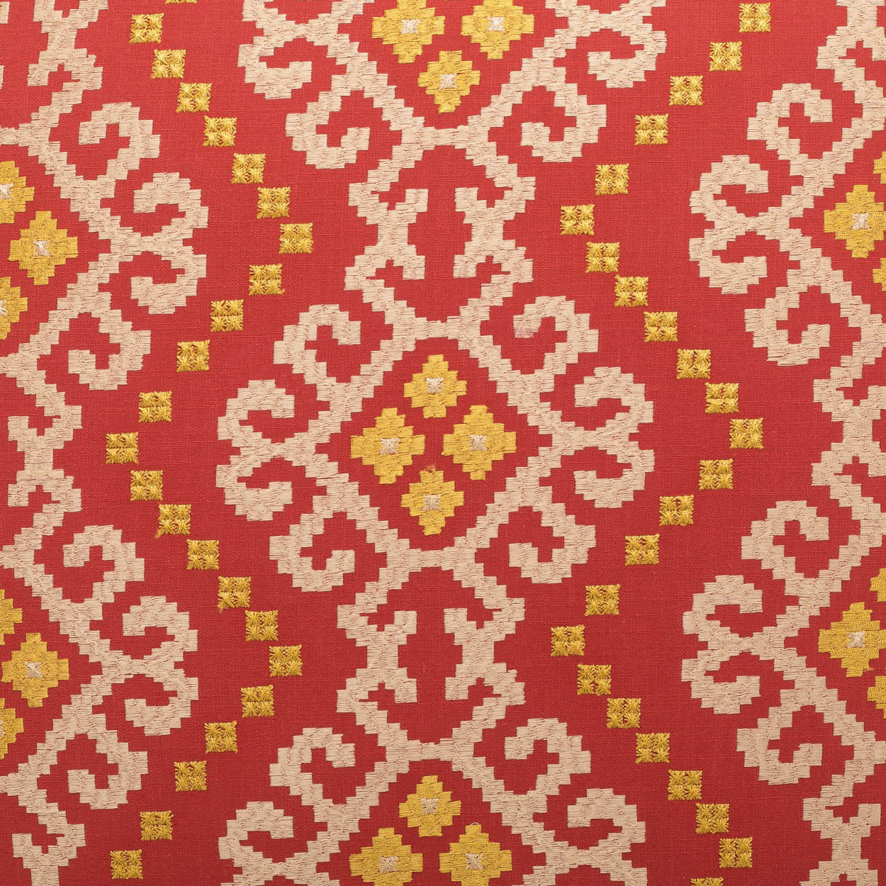 Red fabric with cream scrolling geometric motifs and gold diamond centers in a repeating kilim-like pattern.