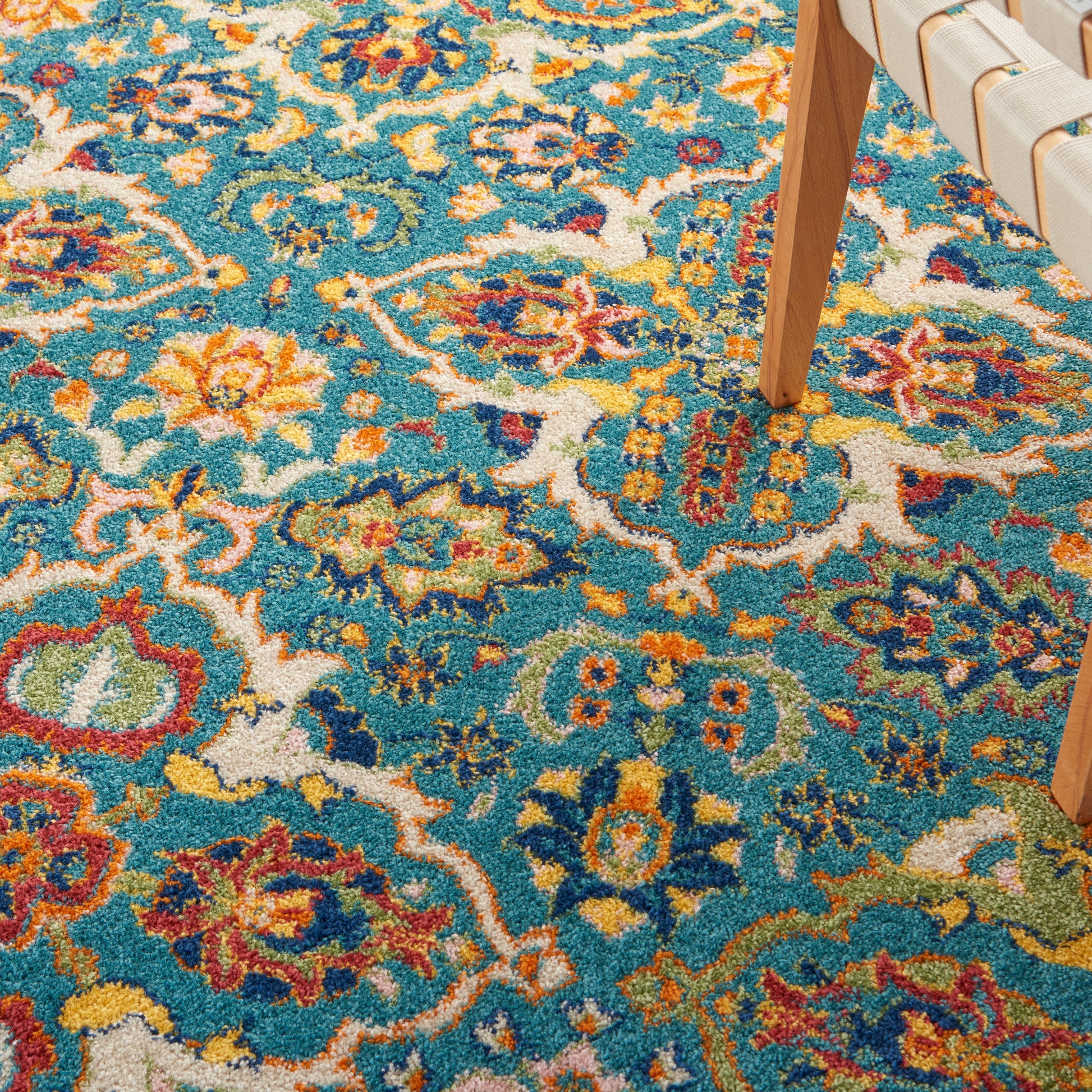 Vibrant Bohemian-style rug with teal base and orange, yellow, red floral patterns; wooden chair leg visible.