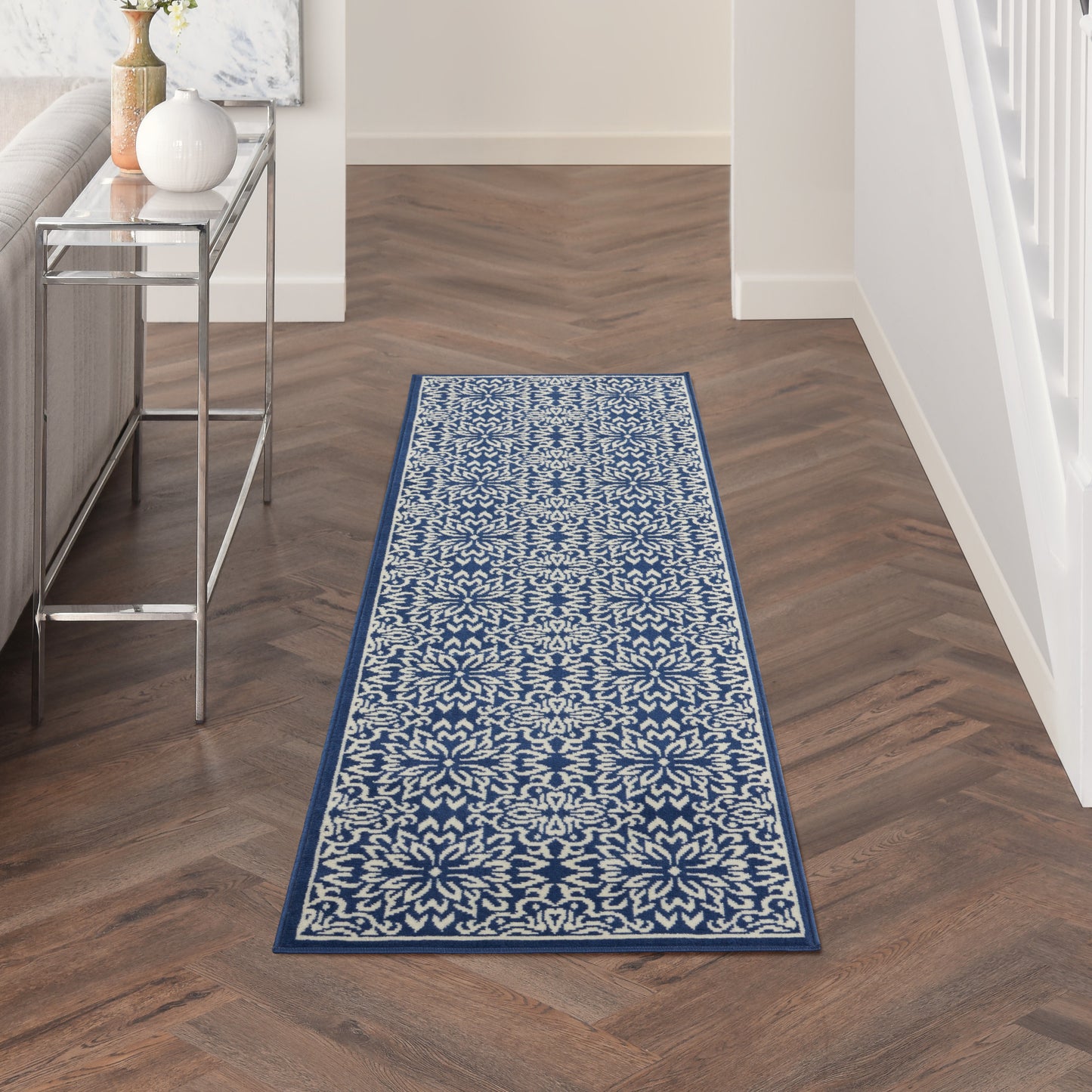 Blue and white floral patterned runner rug with ornate medallion border in a wood-floored hallway.