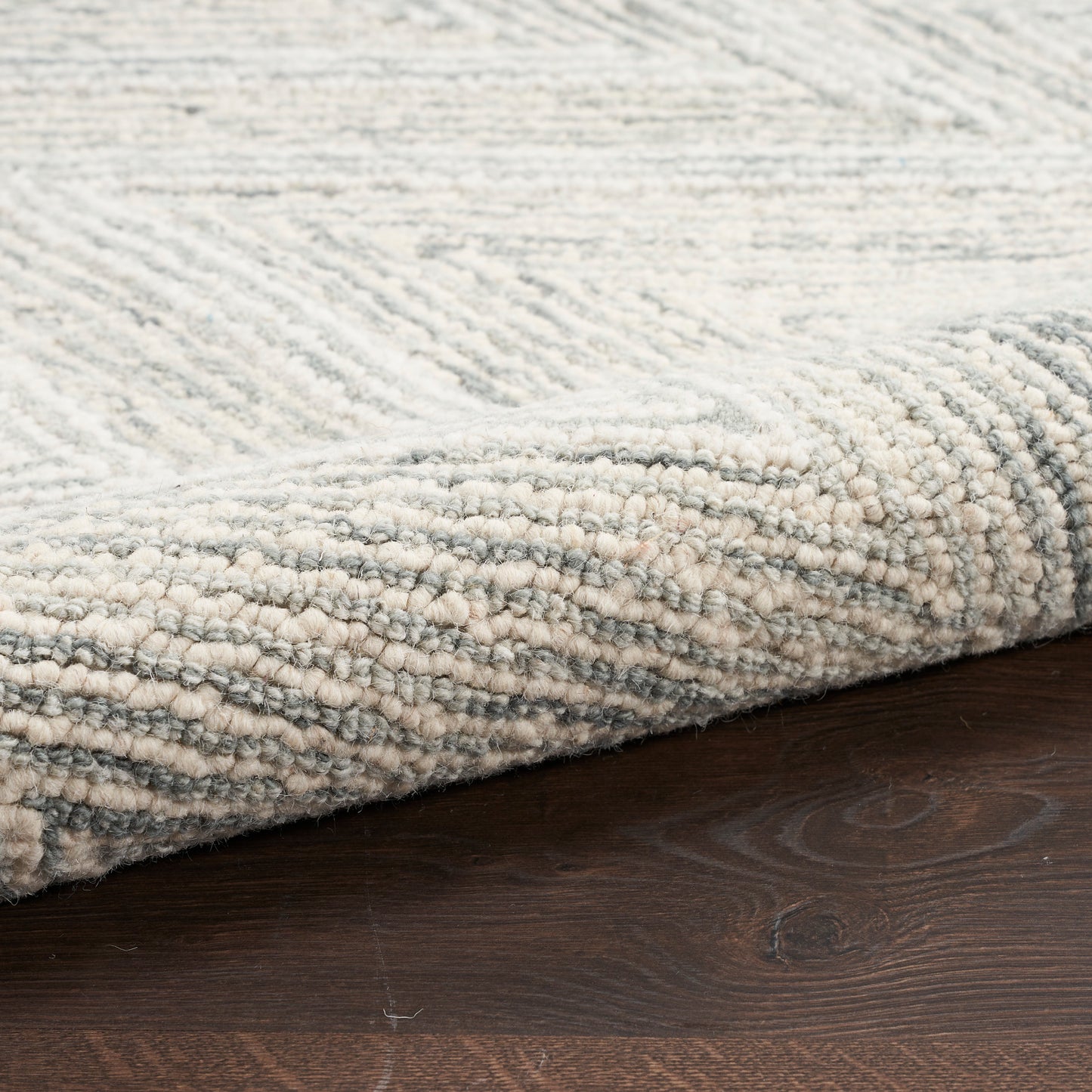 Edge of a light gray and ivory textured rug with a looped pile on dark wood floor.