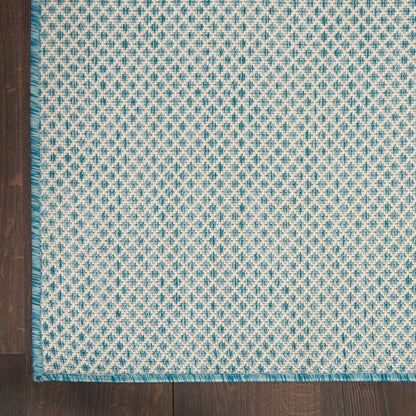 Woven rug with turquoise and cream small diamond pattern, teal fringe on dark wood floor.