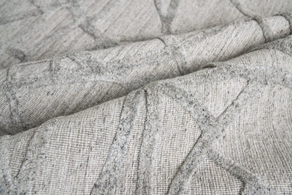 Light gray indoor rug with textured surface and geometric triangular stitching, folded and draped.