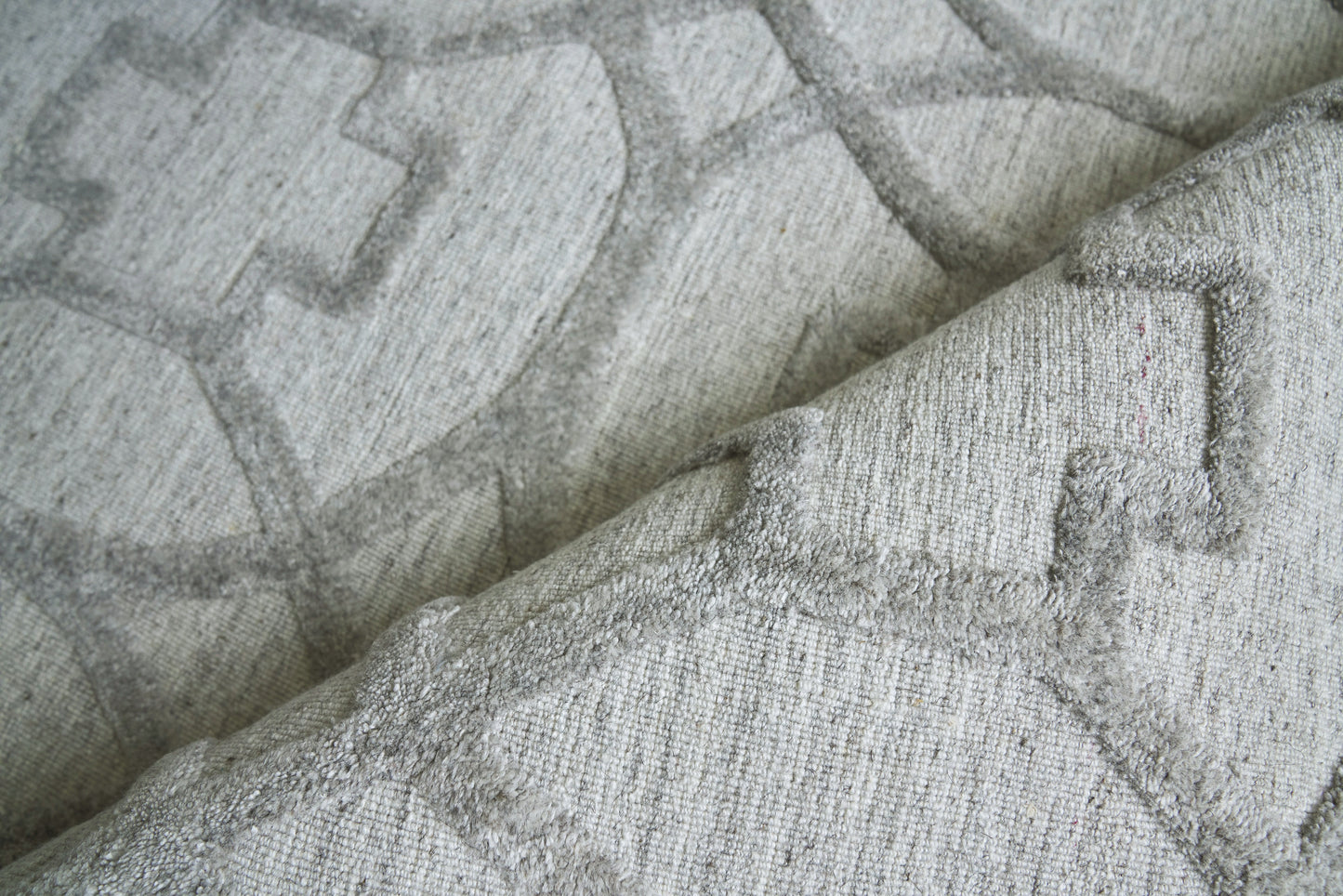 Light gray geometric woven rug with a raised pattern and soft textured pile; folded edge visible.