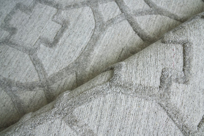 Light gray geometric woven rug with a raised pattern and soft textured pile; folded edge visible.