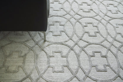 Partial view of a light gray geometric rug with interlocking circle and square patterns, dark sofa leg on the left.