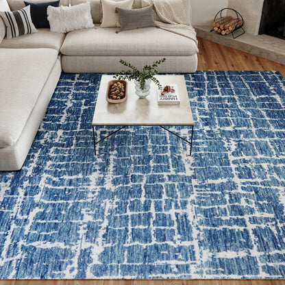 Blue and white abstract rug under beige sectional sofa; marble-top coffee table with black metal legs, vase, bowl & book.
