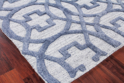 Light gray area rug with a blue geometric interlocking pattern on dark hardwood floor.