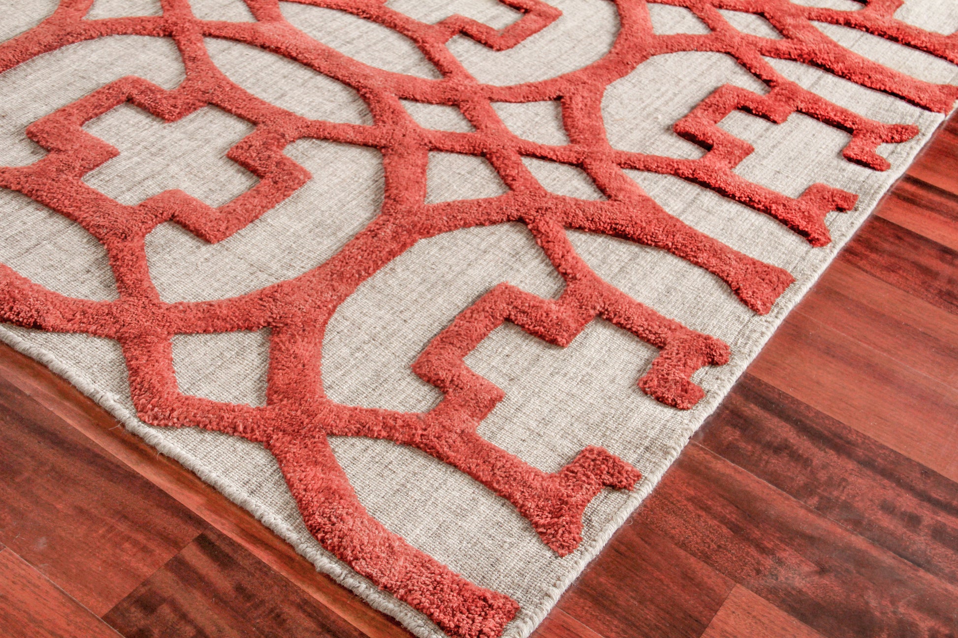Beige hand loomed indoor rug with raised red geometric lattice pattern on wood floor.