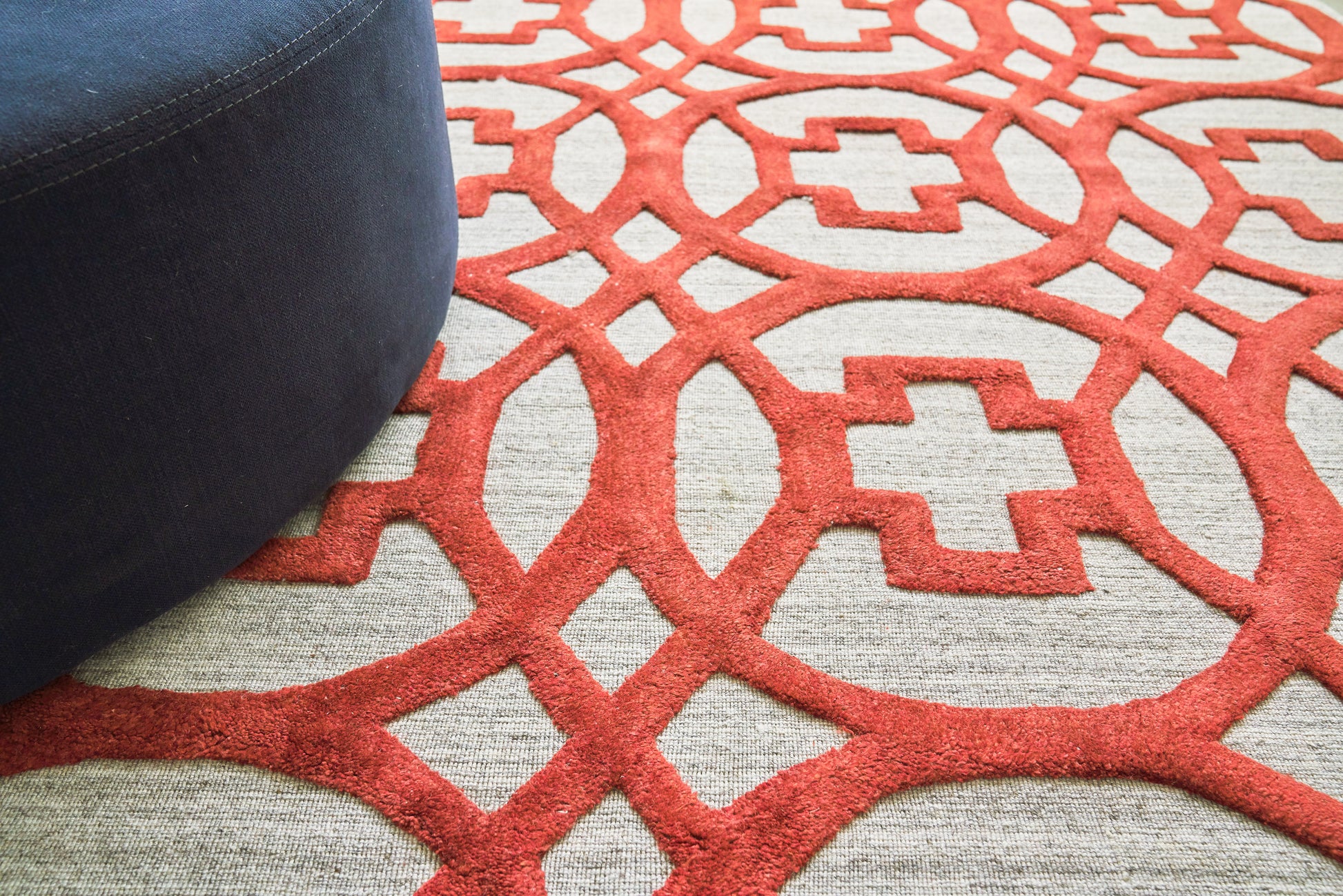 Close-up of a red geometric lattice rug on a light gray base with a dark blue ottoman edge.