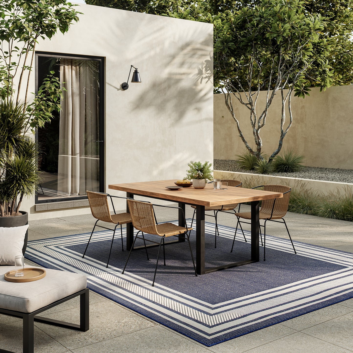 Outdoor modern dining scene with a rectangular wooden table, black metal legs, wicker chairs, on a blue-striped outdoor rug.
