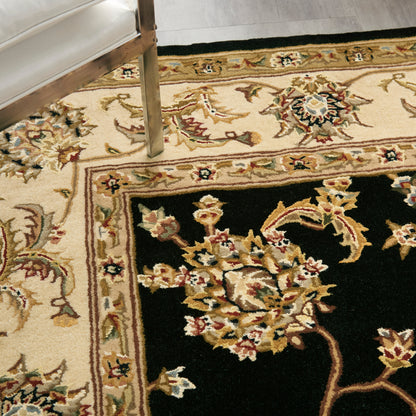 Oriental-style area rug with black central field and gold/red floral motif; ivory/beige border; wooden furniture leg visible.