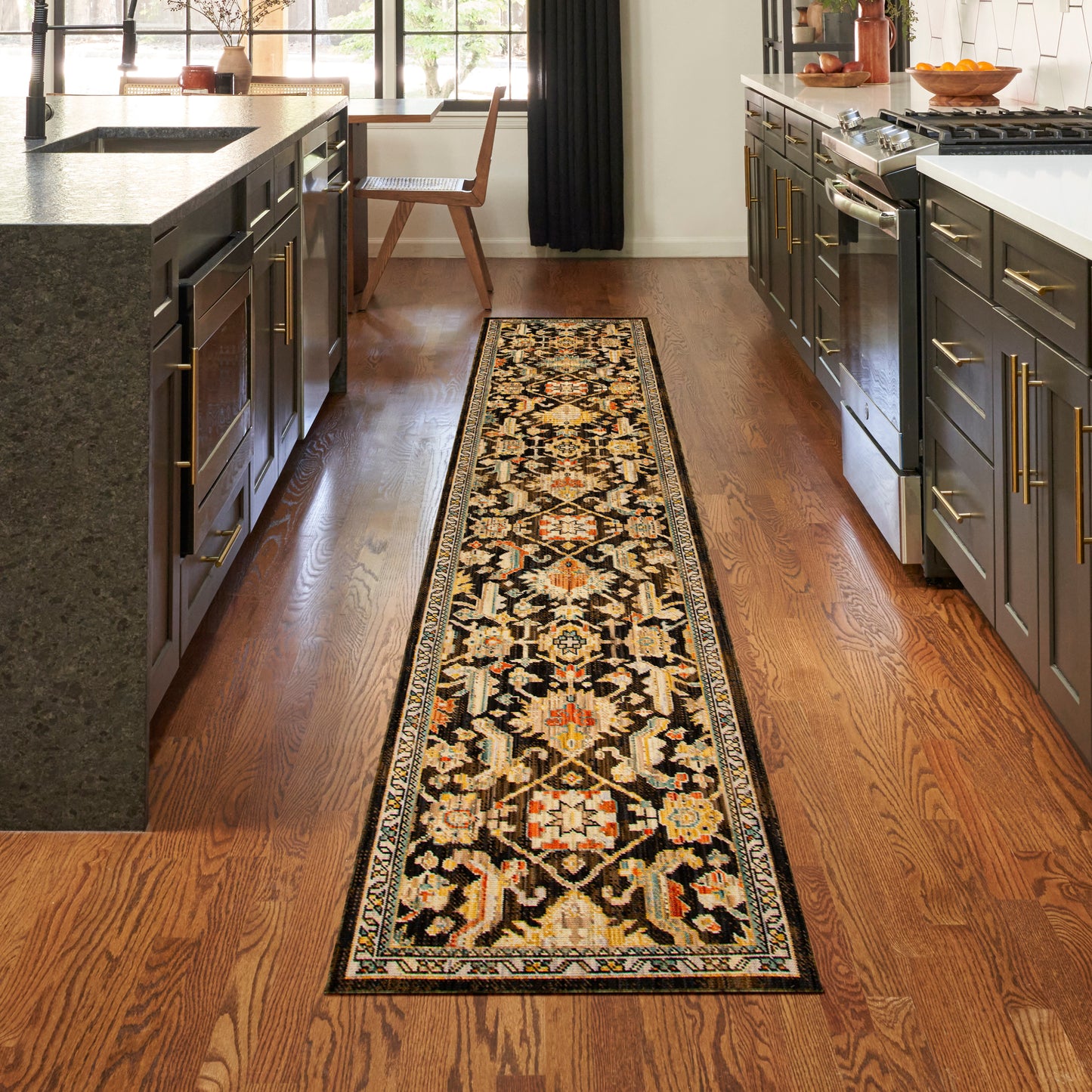 Oriental-style runner rug with geometric motifs in black, cream, rust on a hardwood kitchen floor between dark gray cabinets.