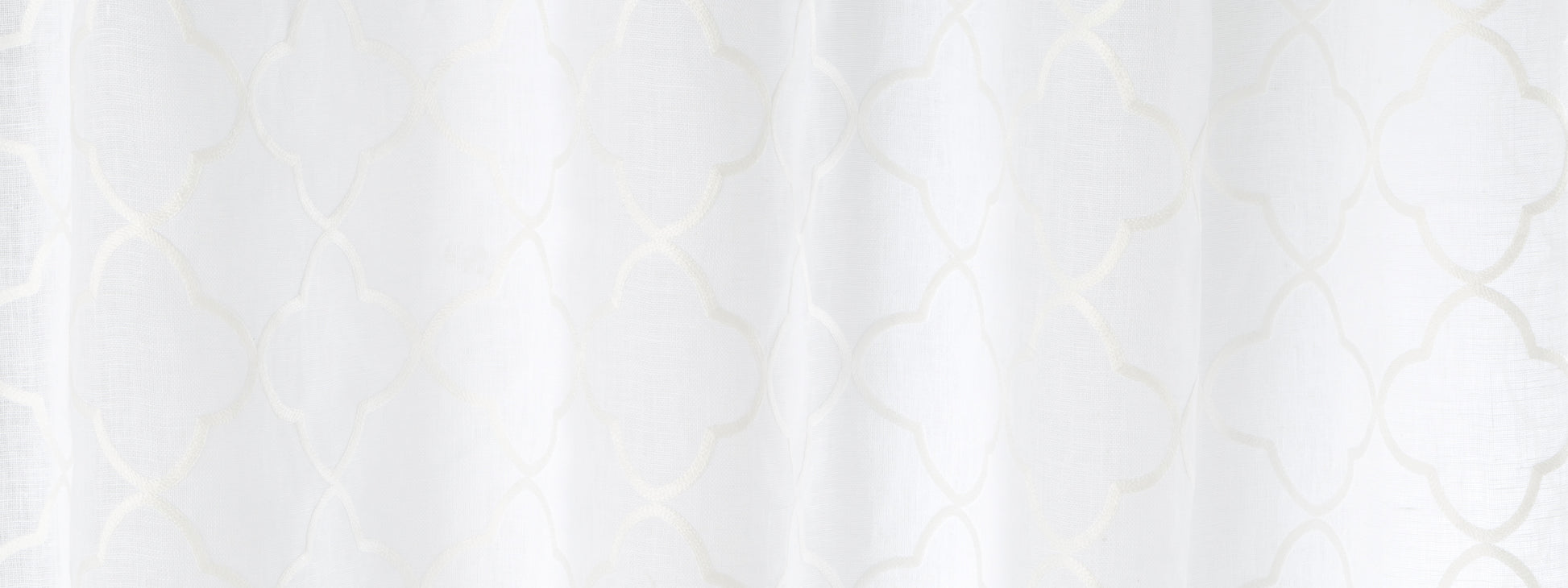 White sheer curtain with delicate quatrefoil lattice pattern and soft draped folds.