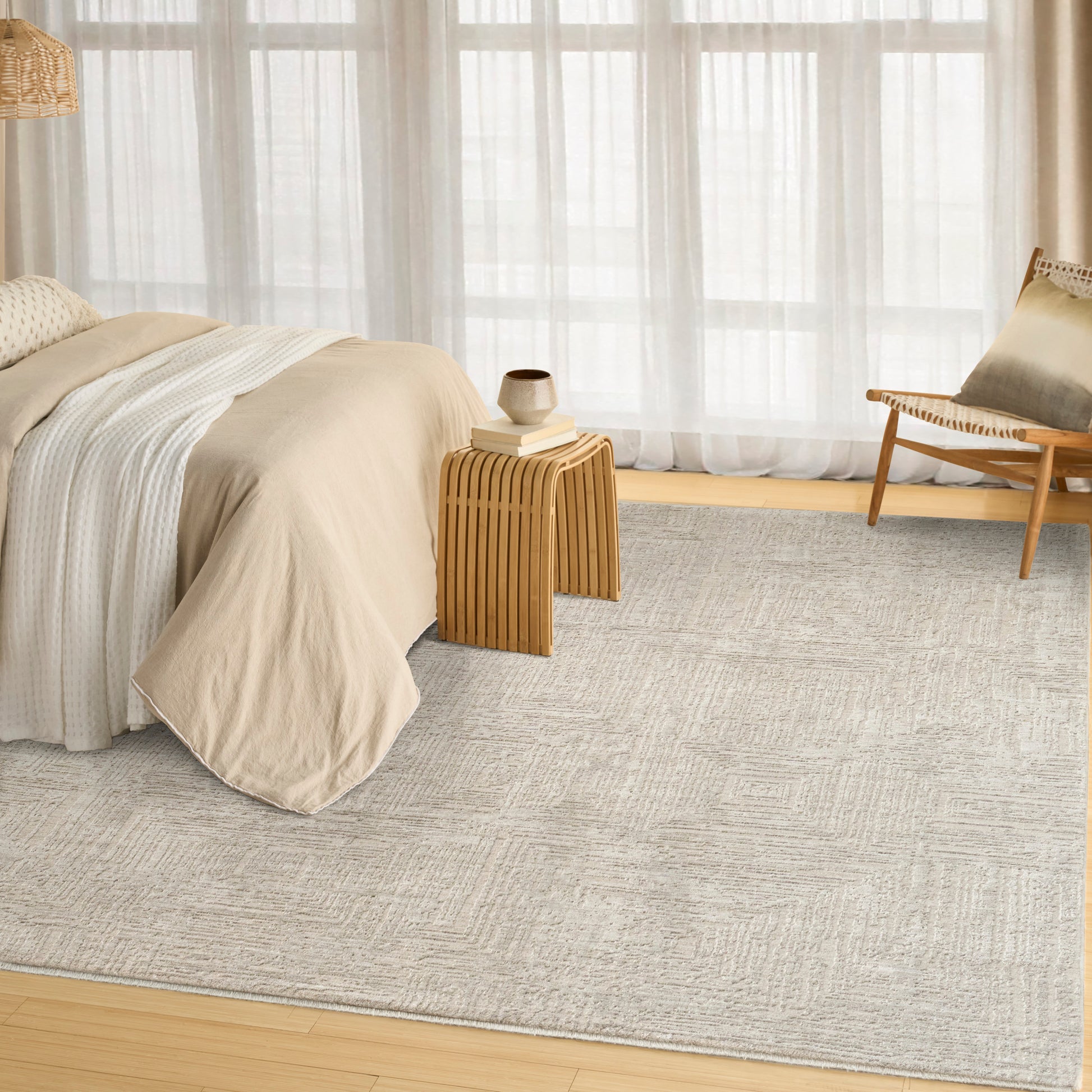 Neutral beige bedroom with linen bedding, light gray textured rug, wooden nightstand and chair under sheer curtains.