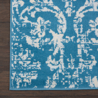 Teal-blue rug with white damask floral motif and slim border on a dark wood floor.