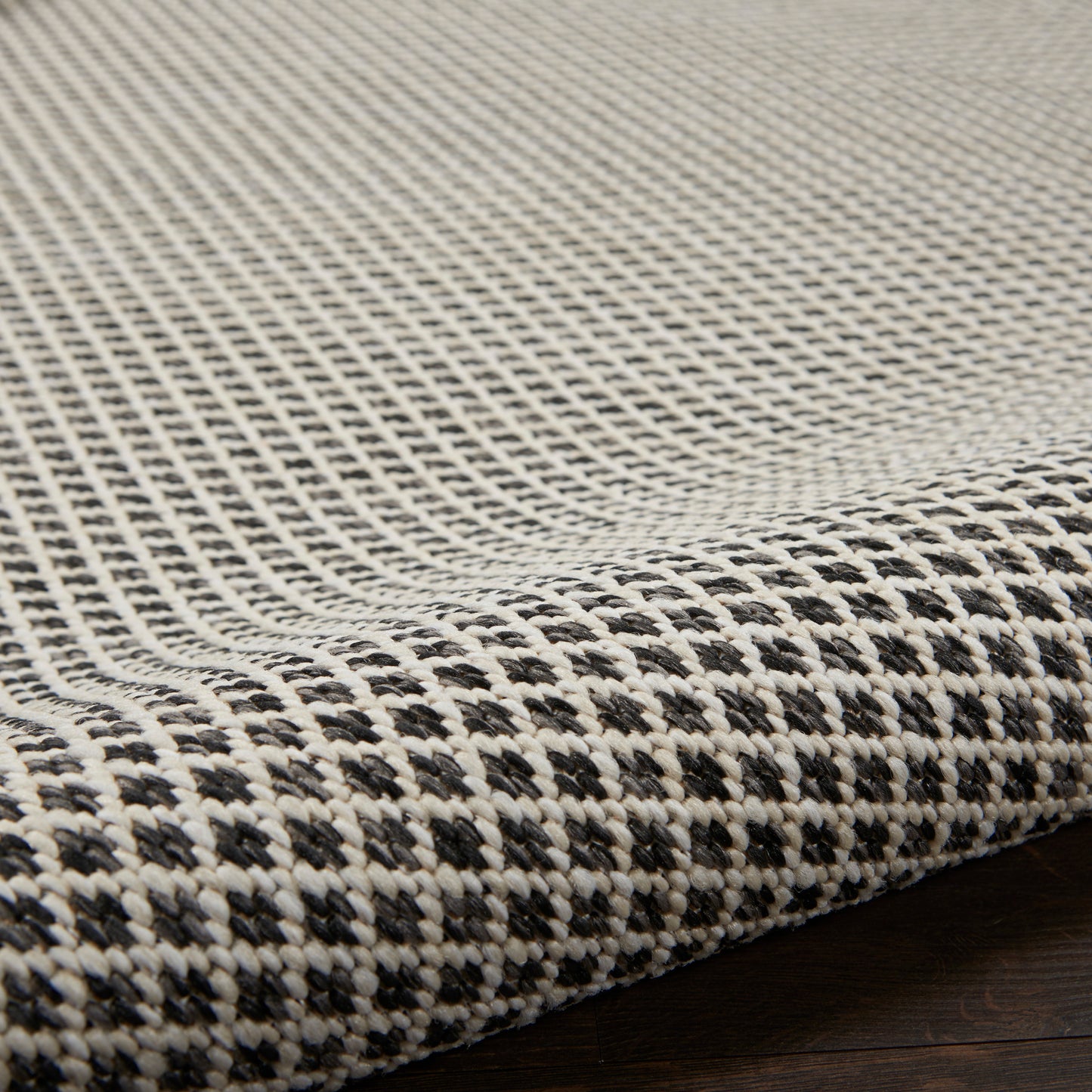 Close-up of a black-&-white woven rug with a tight checker pattern and textured edge on a dark wood floor
