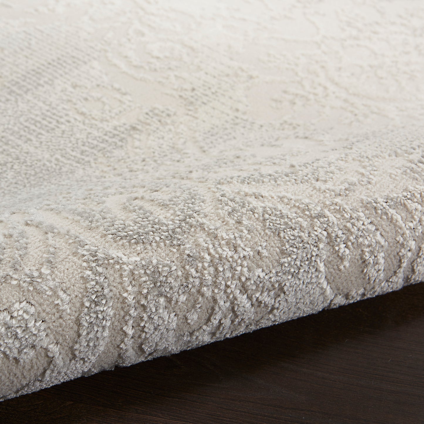 Beige textured area rug with a subtle pattern on a dark wood floor; plush cut-pile with edge visible.