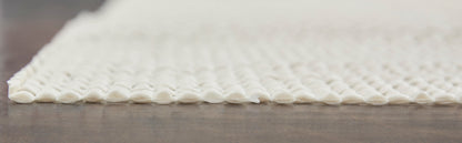 White woven rug with bubble-loop fringe along edge on a wooden floor.