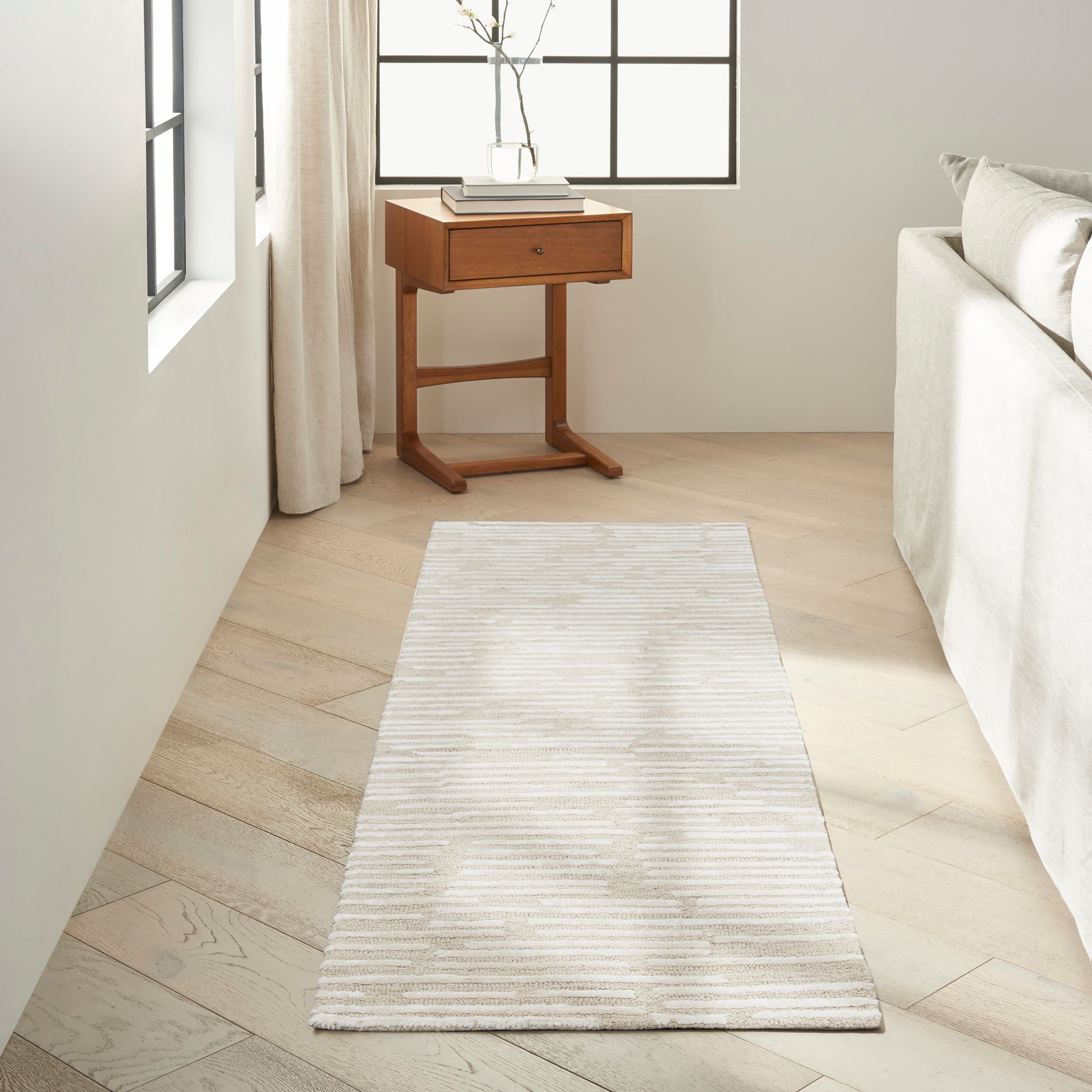 Neutral beige striped rug runner on light wood floor beside a cream sofa and small wooden side table.