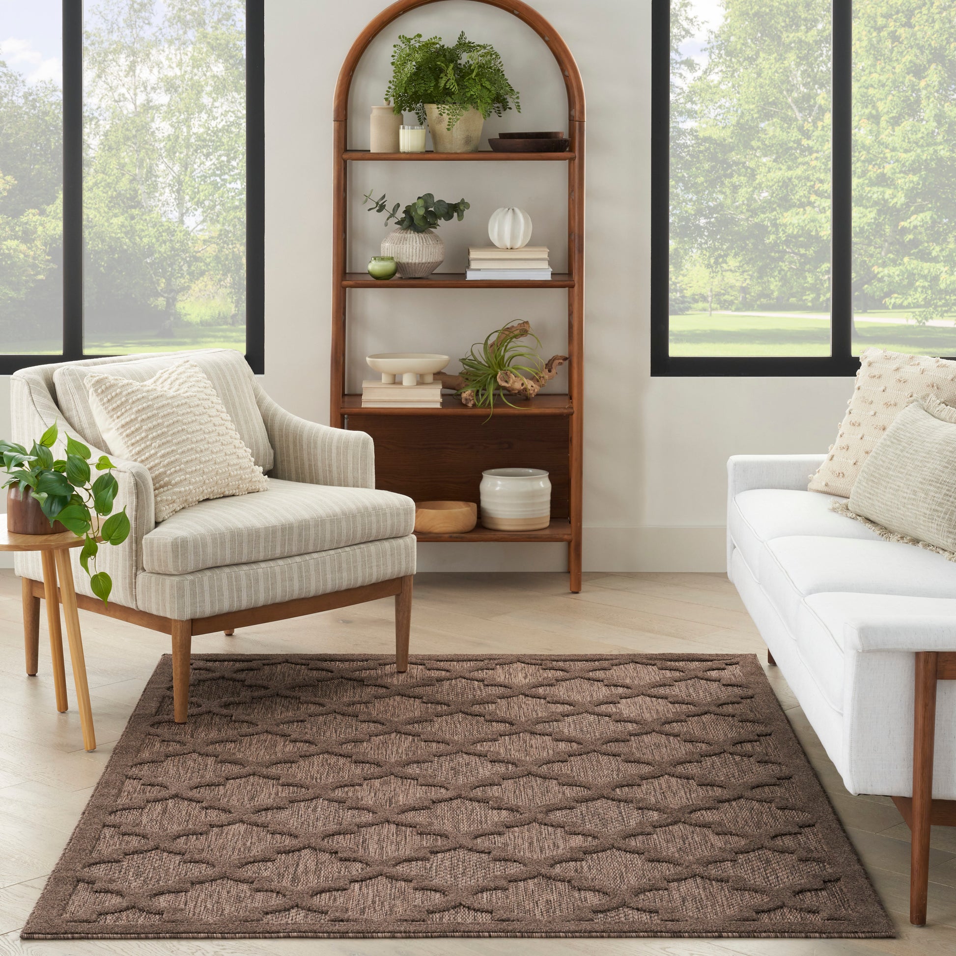 Wood arched bookshelf with plants and decor; beige armchair, white sofa, and brown textured rug in a sunlit living room.