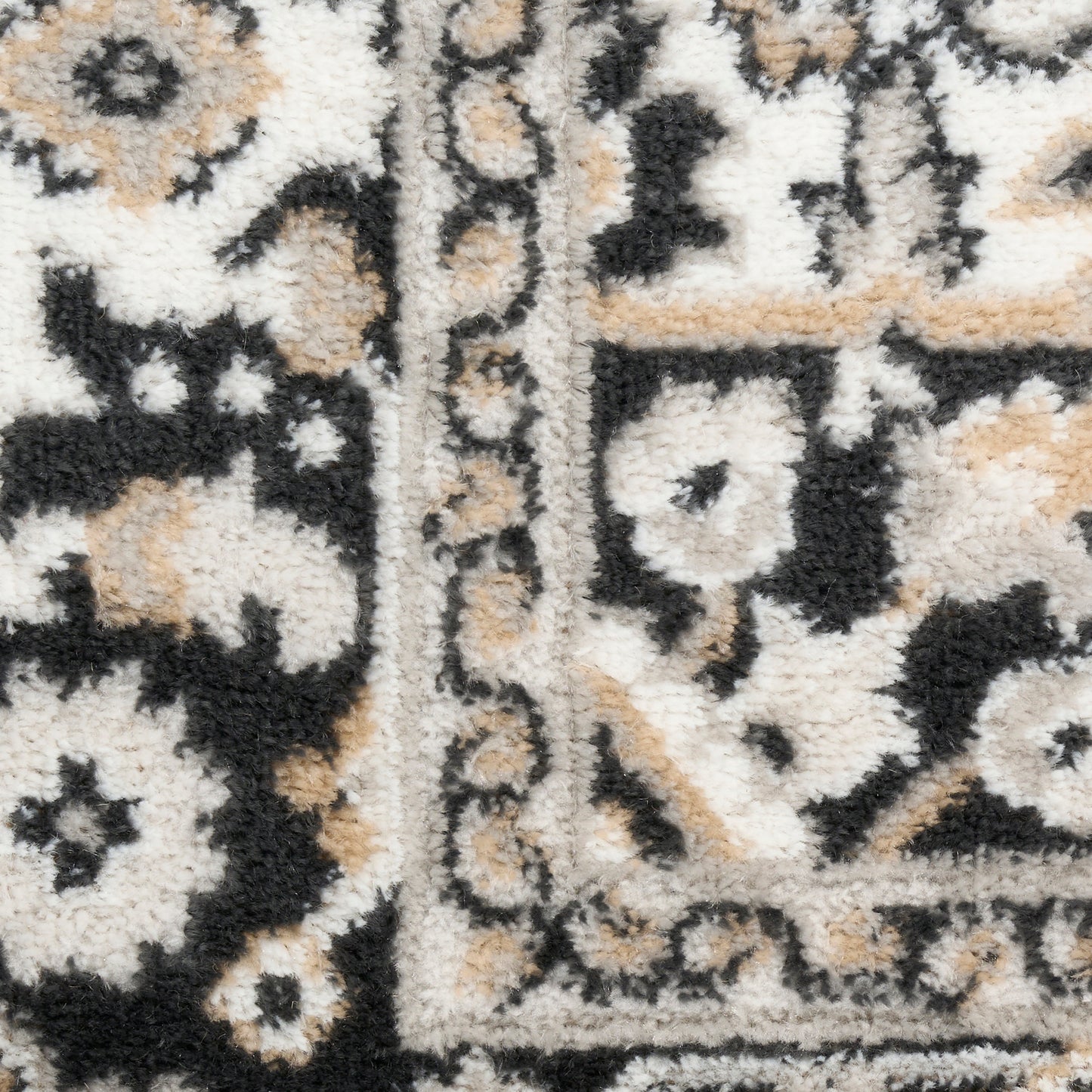 Close-up of a cream, black and tan oriental rug with floral motifs and a bordered edge, plush pile.