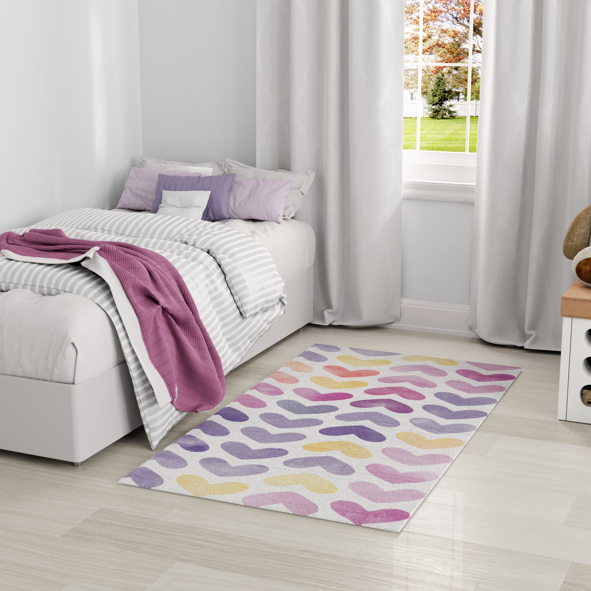 Cozy bedroom with a white bed, gray striped duvet, pink throw, lilac pillows, & pastel wavy rug on light wood flooring.