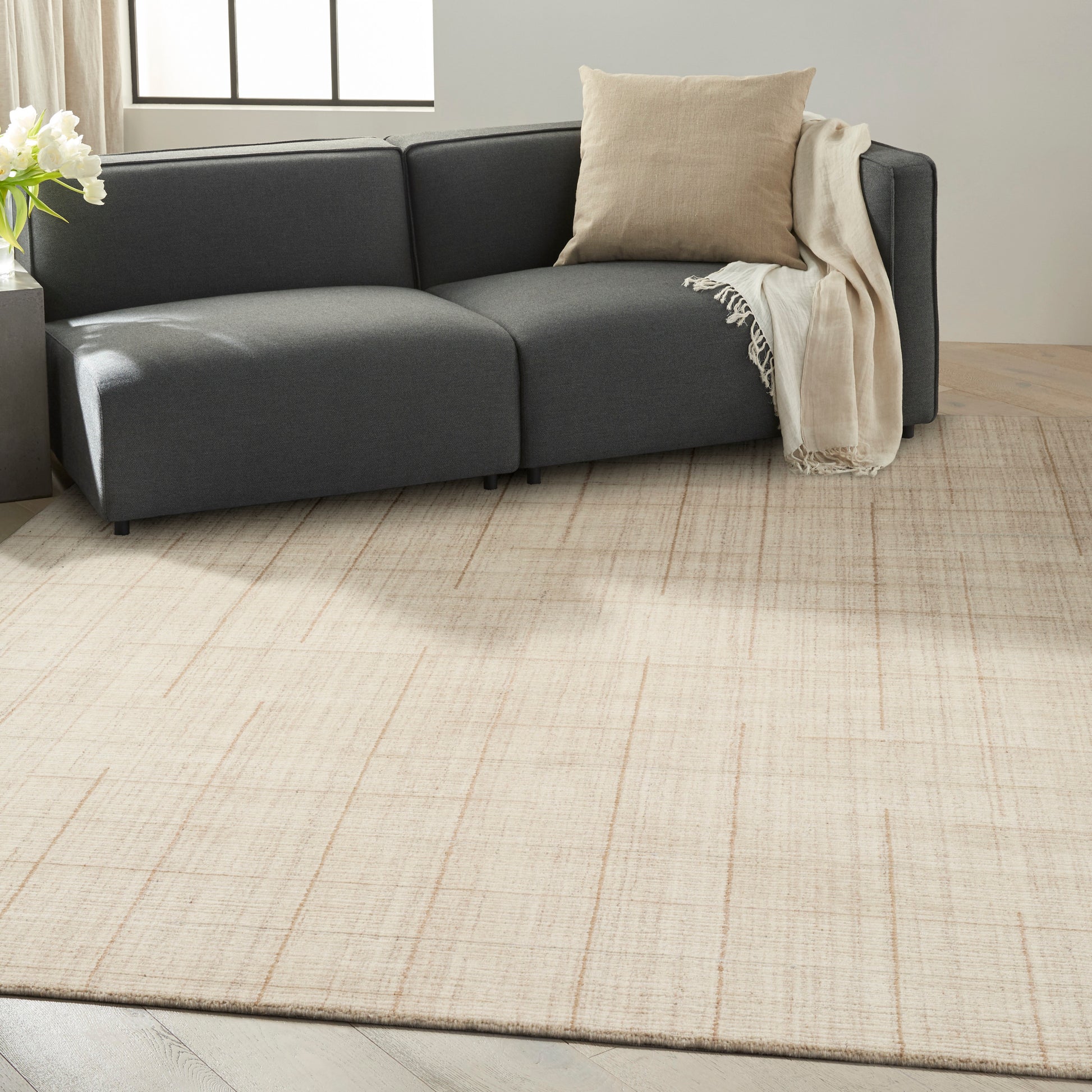 Dark gray sectional sofa on a light beige rug with a beige pillow and cream throw in a bright living room.