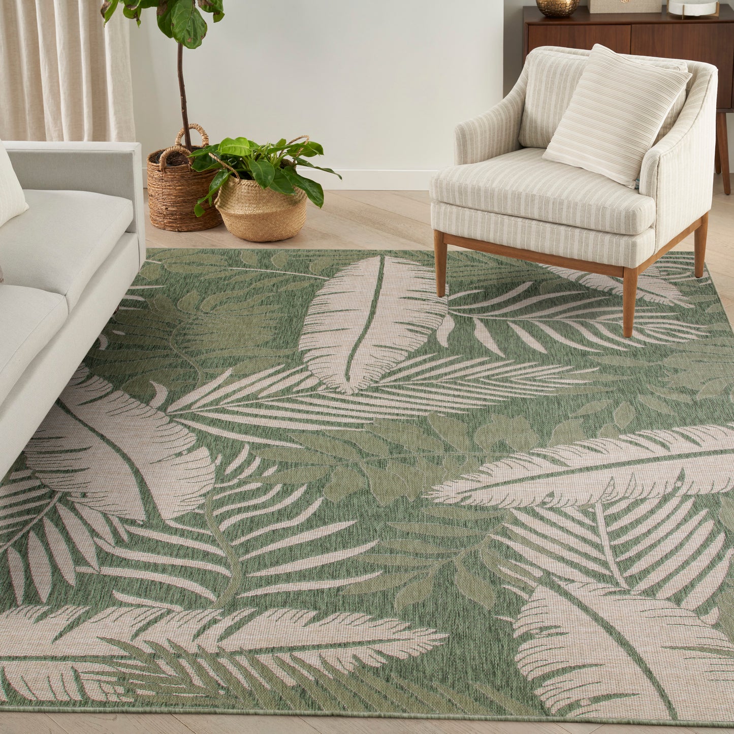 Cozy living room with a textured green tropical leaf rug, beige striped armchair on wood legs, and potted plants.