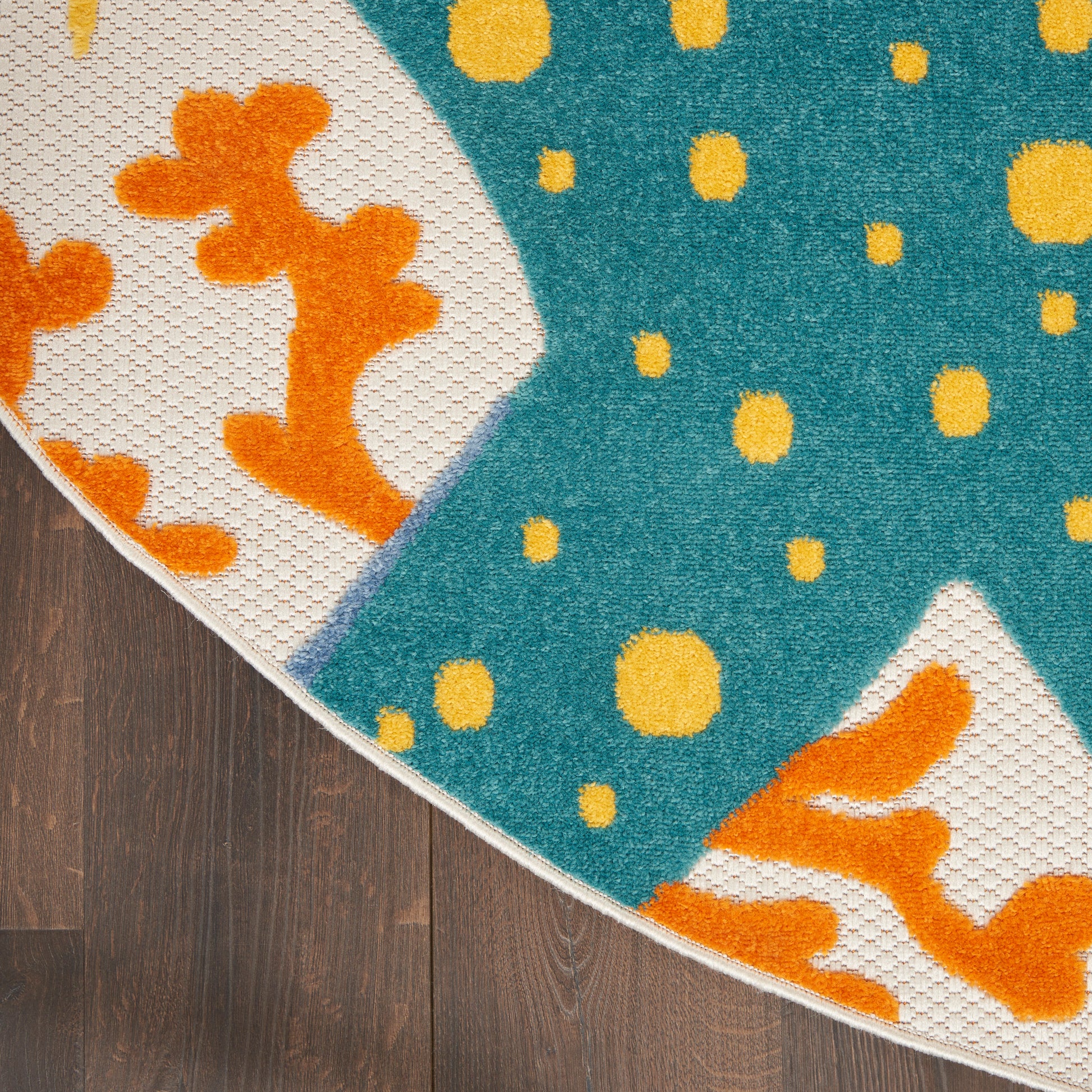 Round rug with teal field and yellow dots; white curved panels with orange coral shapes, fringe on dark wood floor.