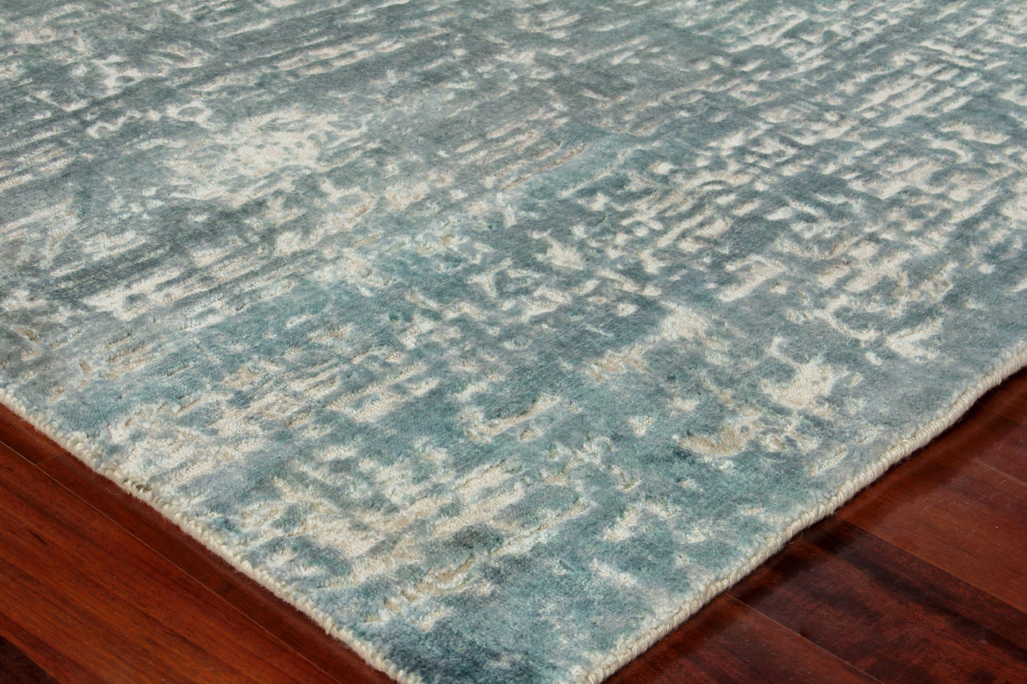 Teal-blue distressed area rug with beige accents on a dark wood floor.