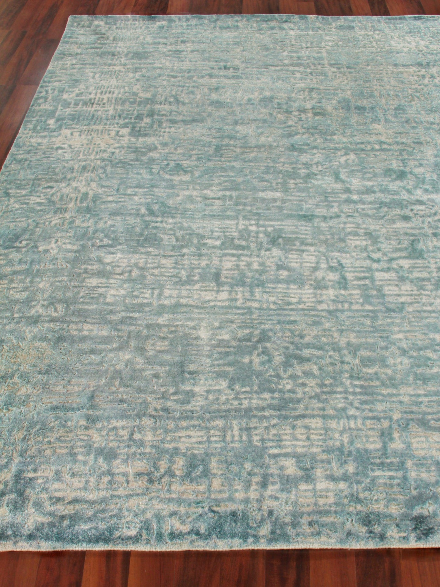 Teal blue distressed-pattern rectangular area rug on wood floor, soft textured look.