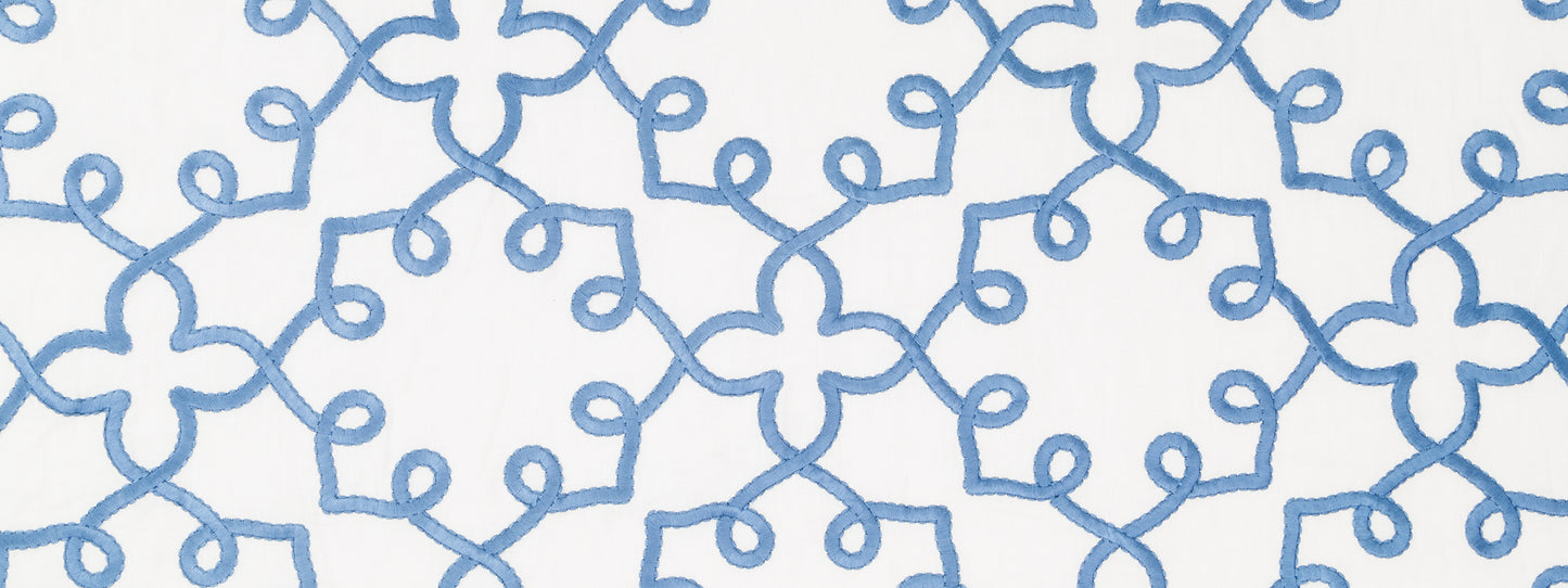 Blue embroidered looped scroll pattern on white fabric; decorative textile with stitched lattice design.