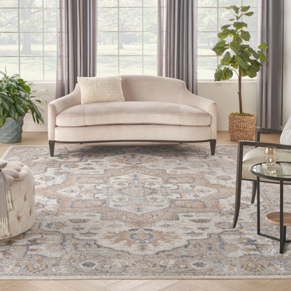 Soft beige curved sofa with dark legs, patterned rug, green plants, gray curtains, and glass coffee table.