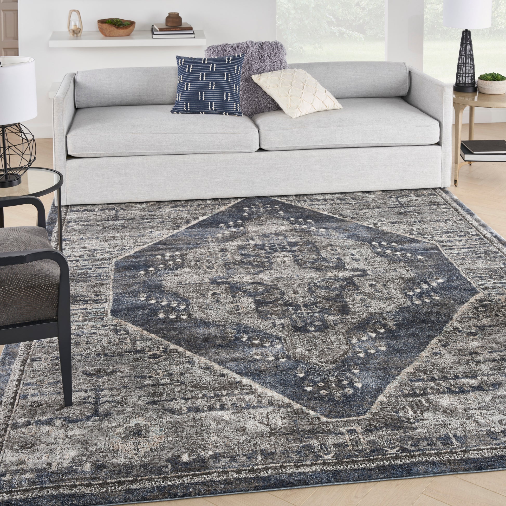 Blue-gray ornate medallion area rug on light wood floor in a modern living room with a light gray sofa and throw pillows.