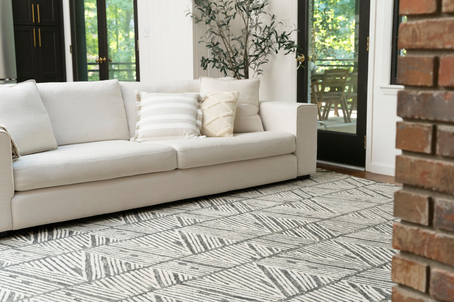 Modern 8' x 10' gray geometric area rug on the floor beside a brick pillar and glass doors.