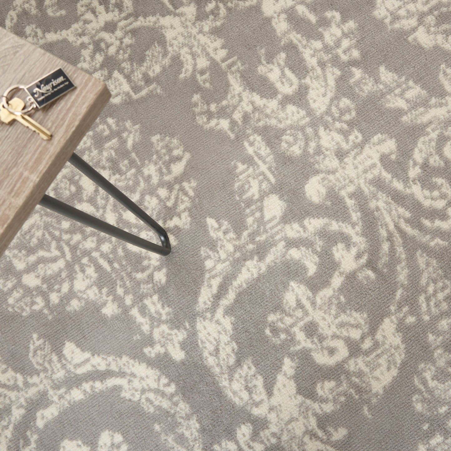 Small light oak end table with black metal hairpin legs; keys on top, resting on a gray floral-patterned rug.
