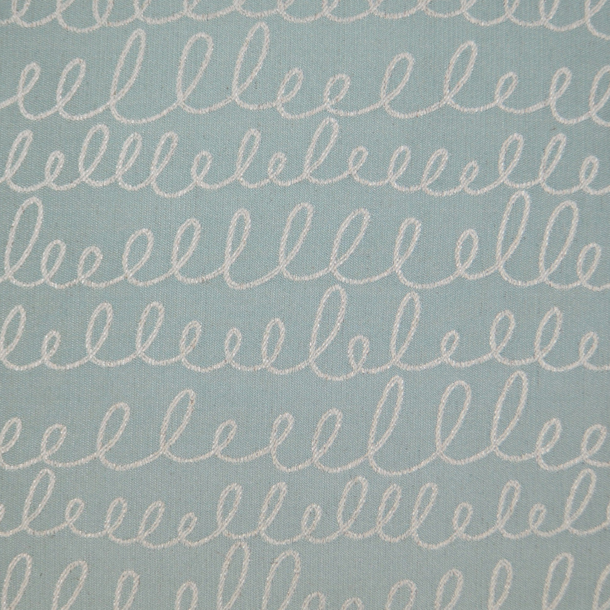 Light blue cotton fabric with repeated white looping cursive embroidery lines.