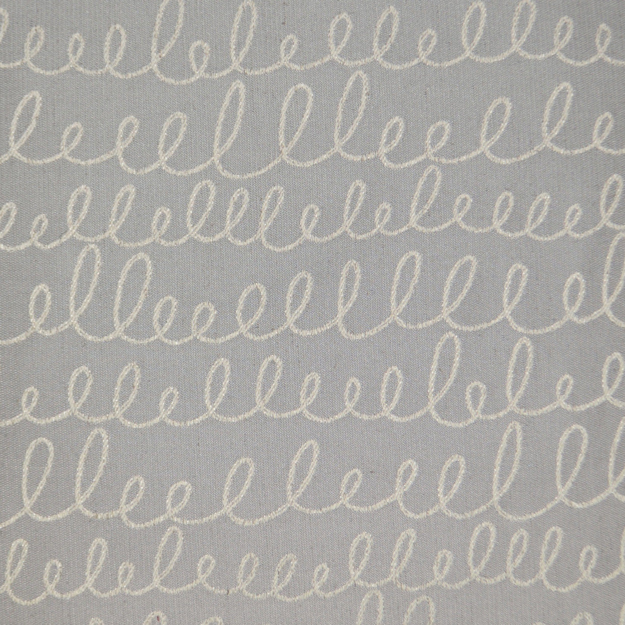 Gray-blue fabric with repeating white looped cursive embroidery motif across.