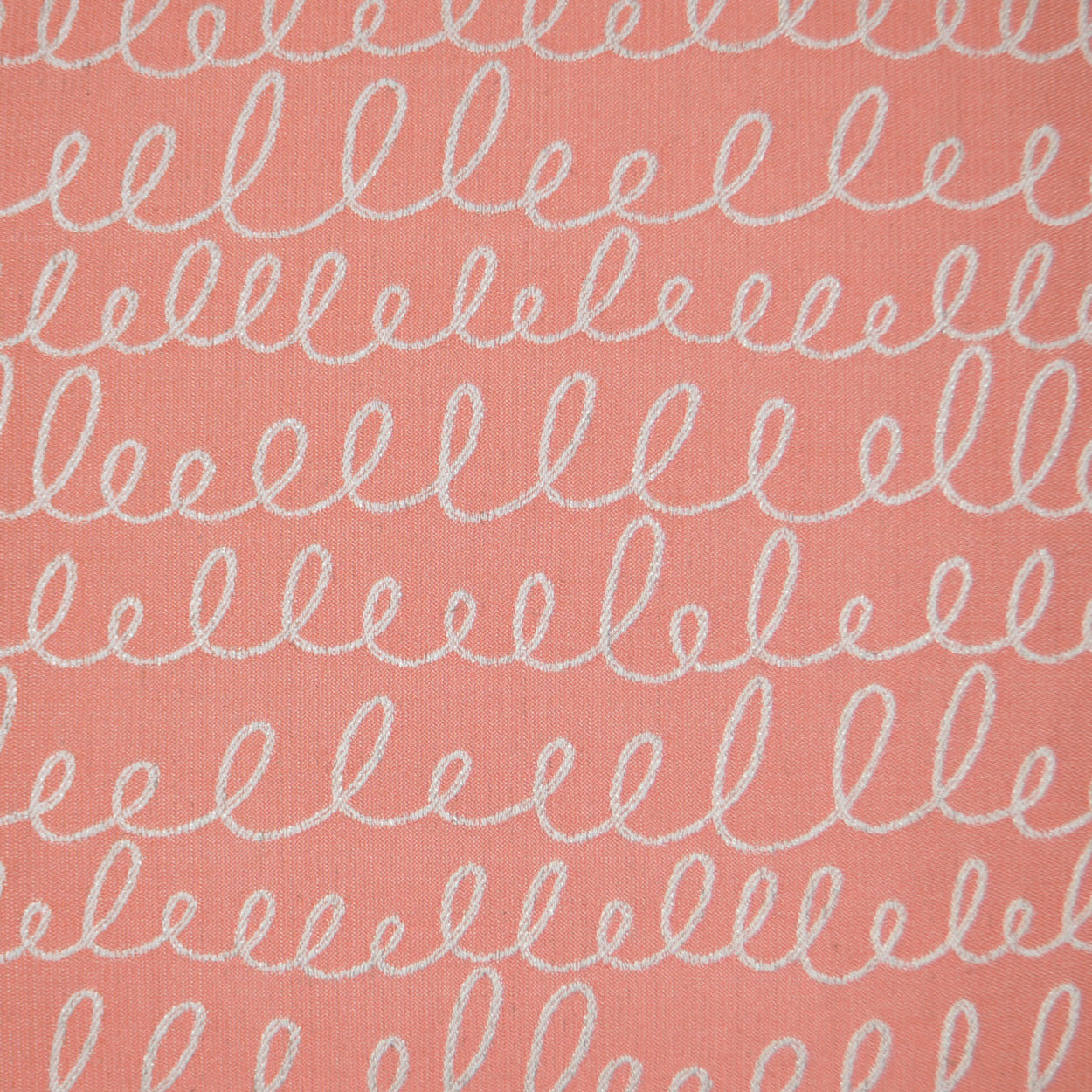 Coral pink fabric with white looping squiggle print in horizontal rows; soft textile texture.