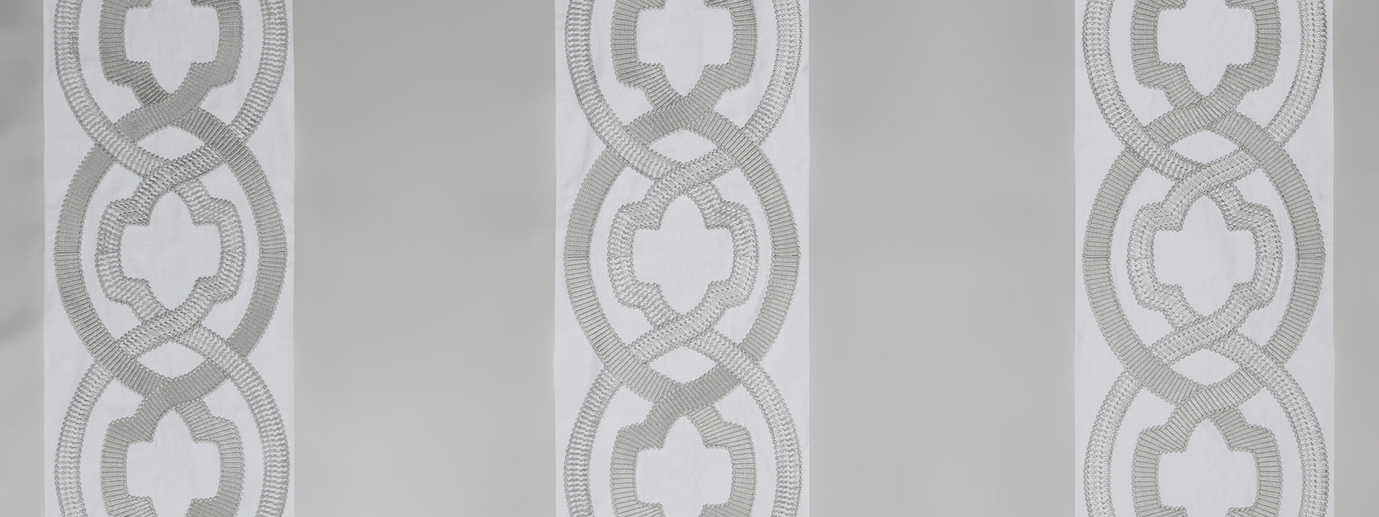 Repeating gray interlocking rings with quatrefoil centers on a light background; wallcovering or textile pattern.