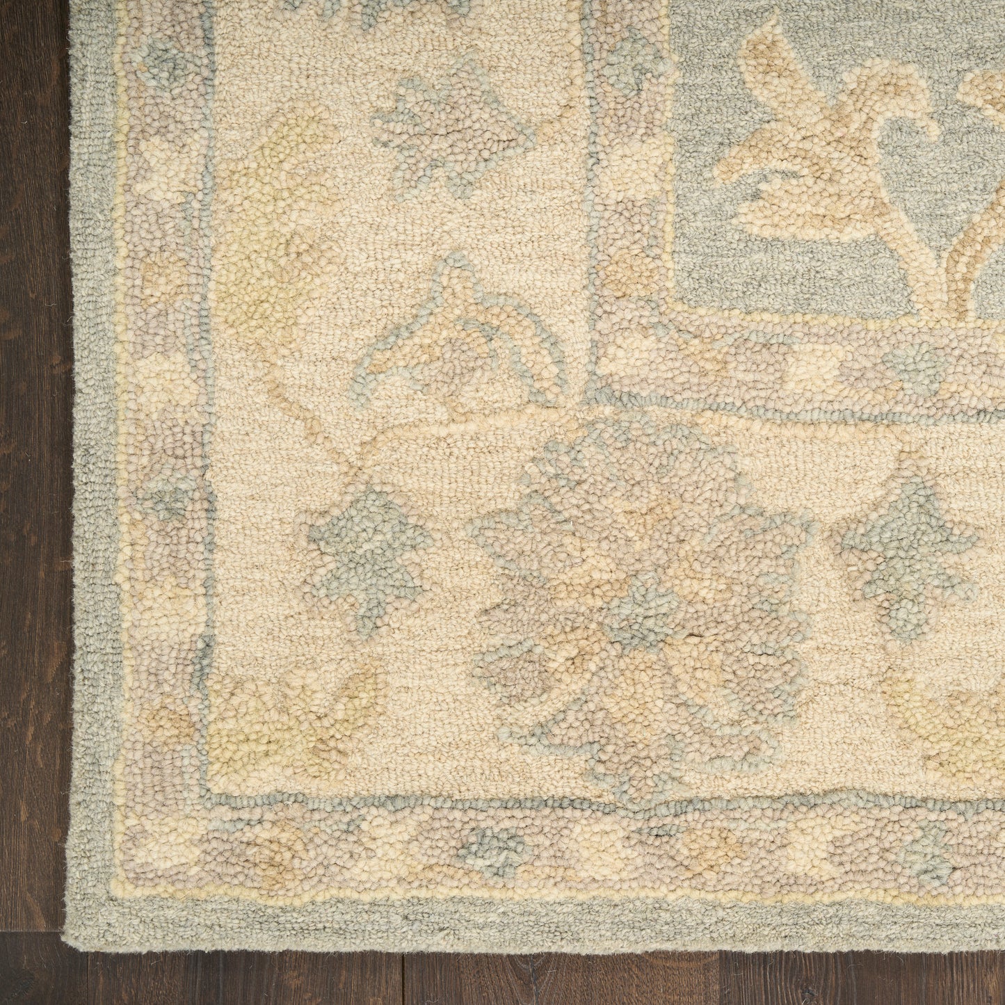 Beige Persian-style rug with pale blue floral border & muted yellow-blue motifs, plush pile on dark wood floor.