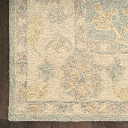 Beige Persian-style rug with pale blue floral border & muted yellow-blue motifs, plush pile on dark wood floor.