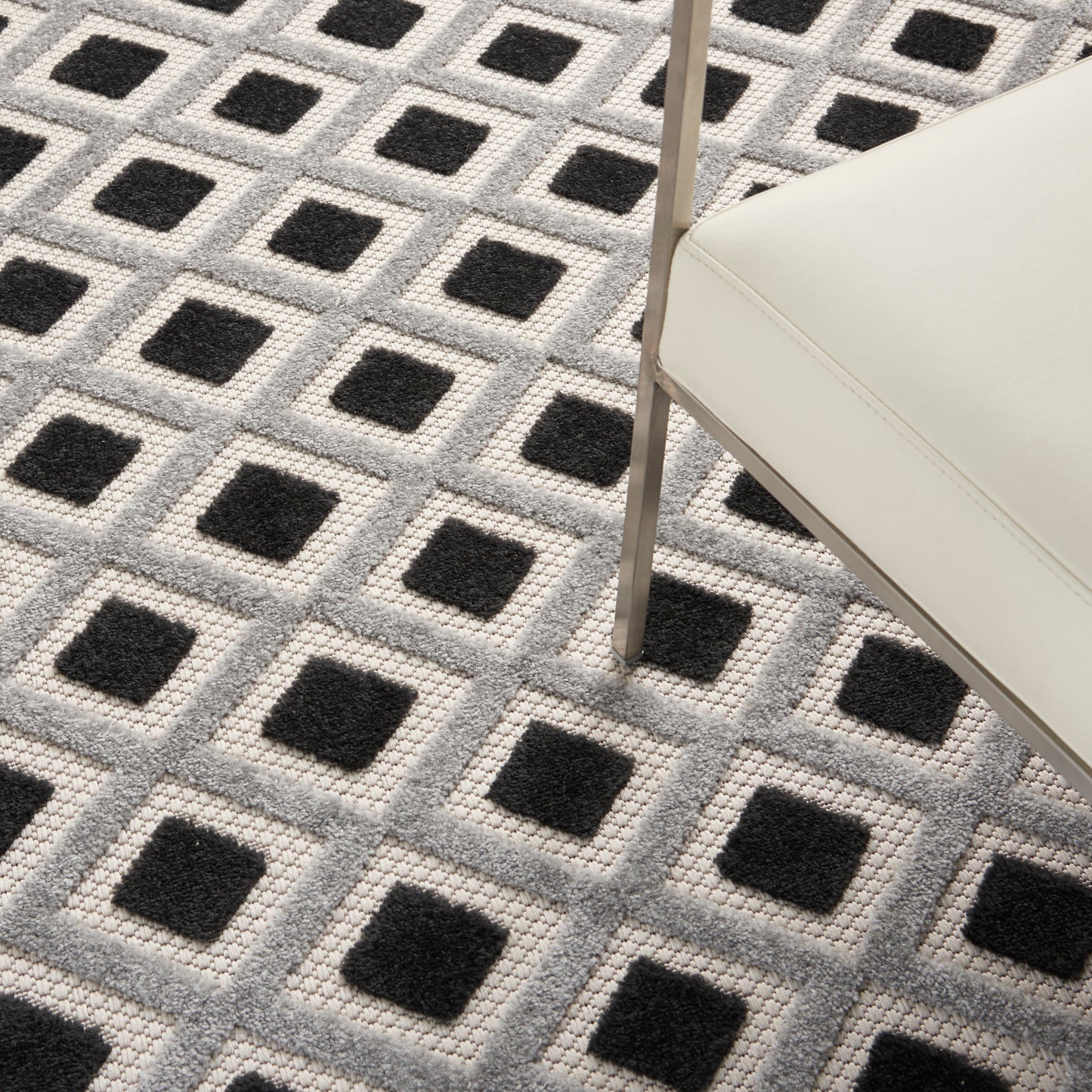 Geometric gray rug with repeating black squares in light gray frames; white upholstered chair with metal leg nearby.