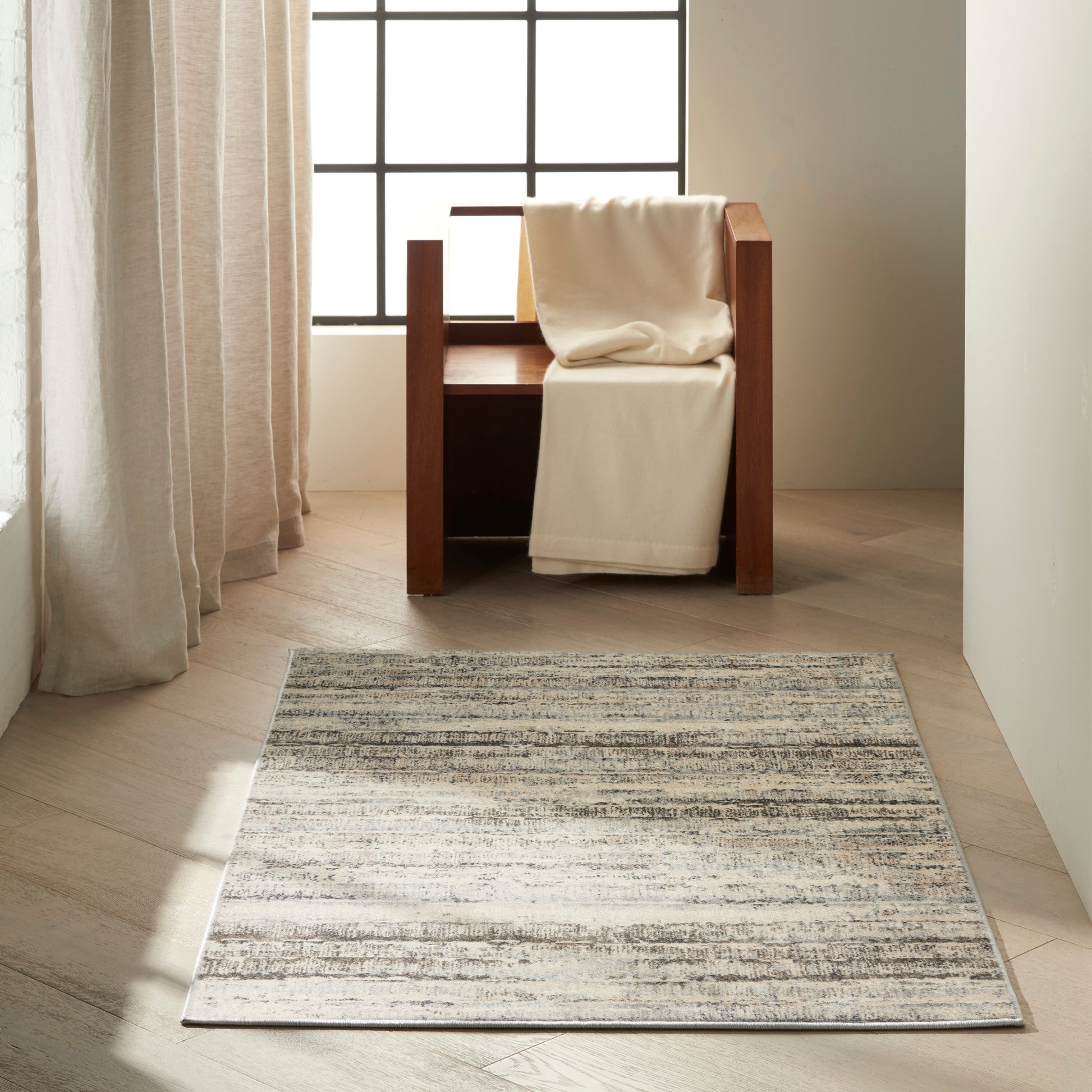 Light gray striped rug on pale wood floor in a bright corner; a cream throw rests on it.