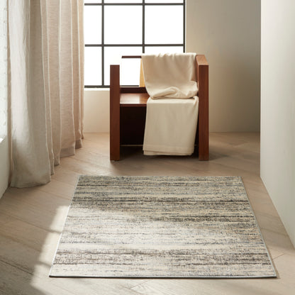 Light gray striped rug on pale wood floor in a bright corner; a cream throw rests on it.