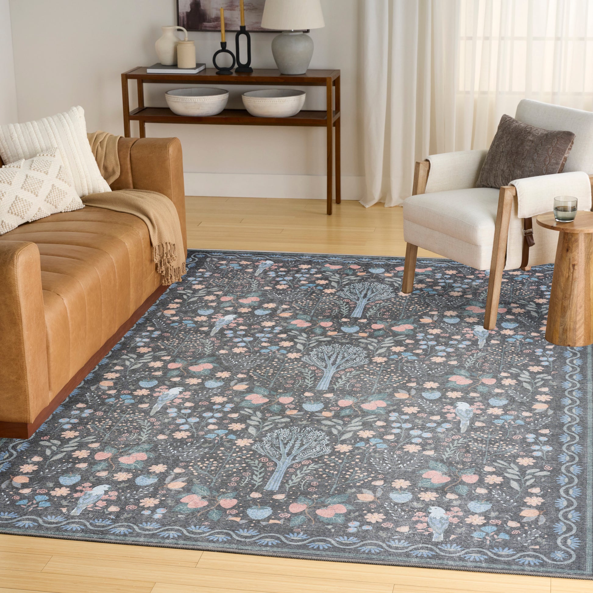Blue floral-patterned area rug with pink accents in a cozy living room; tan leather sofa and white armchair, curtains.